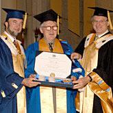 Gordon Legge being presented with an honorary doctorate from University of Montreal president Monsieur Luc Vinet and vice president Jacques Fremont, all three are wearing graduation caps and robes. 