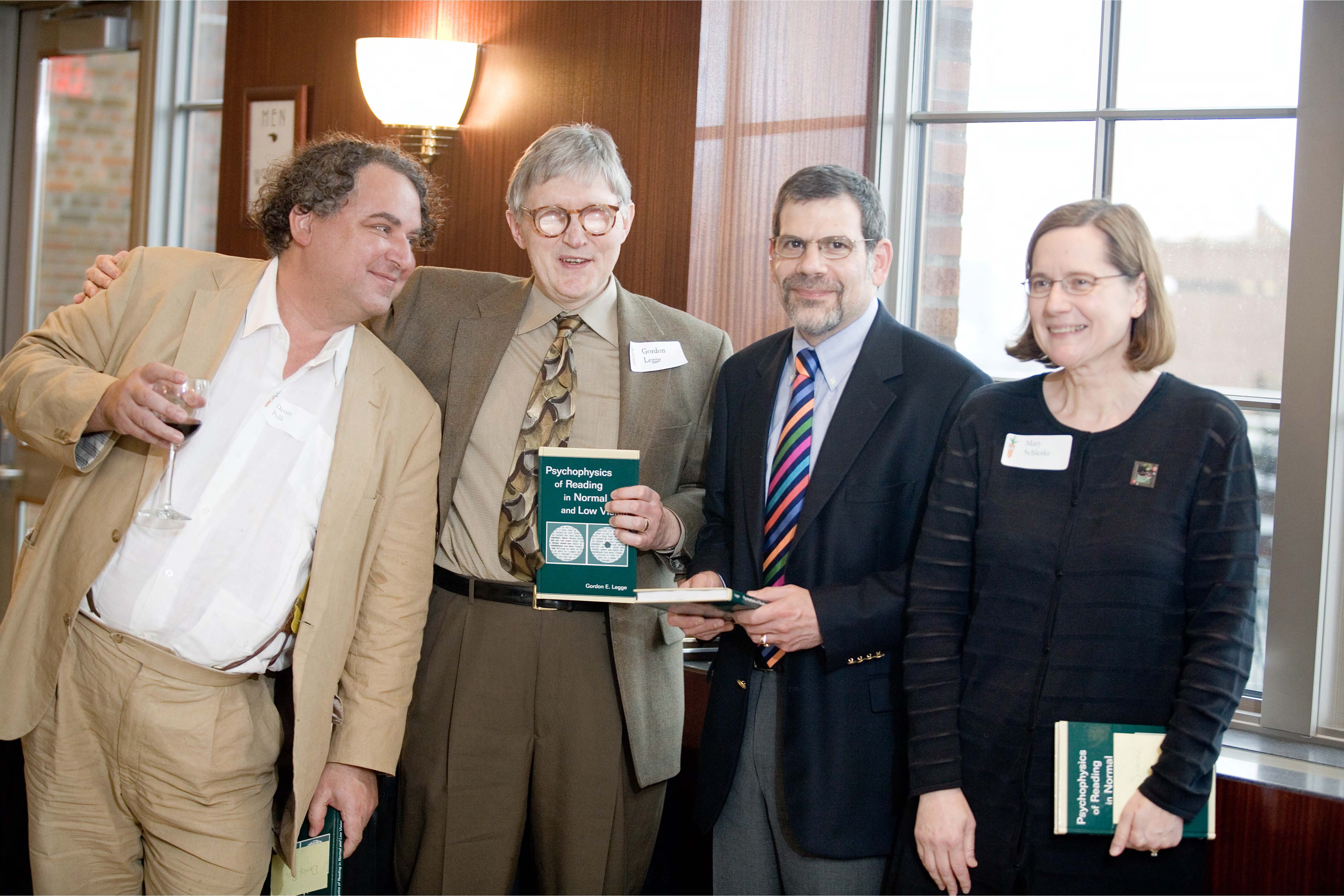 Photo of Gordon Legge holding a copy of his book along with Denis Pelli, Gary Rubin and Mary Schleske. 