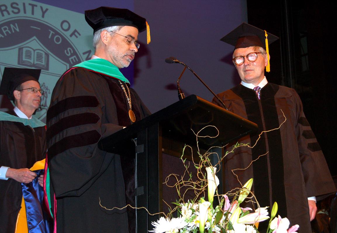 Gordon and President David A. Heath standing on stage, at a podium, wearing graduation robes and caps.