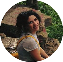 Nilsu Atilgan smiling while sitting on a boulder in a forest.